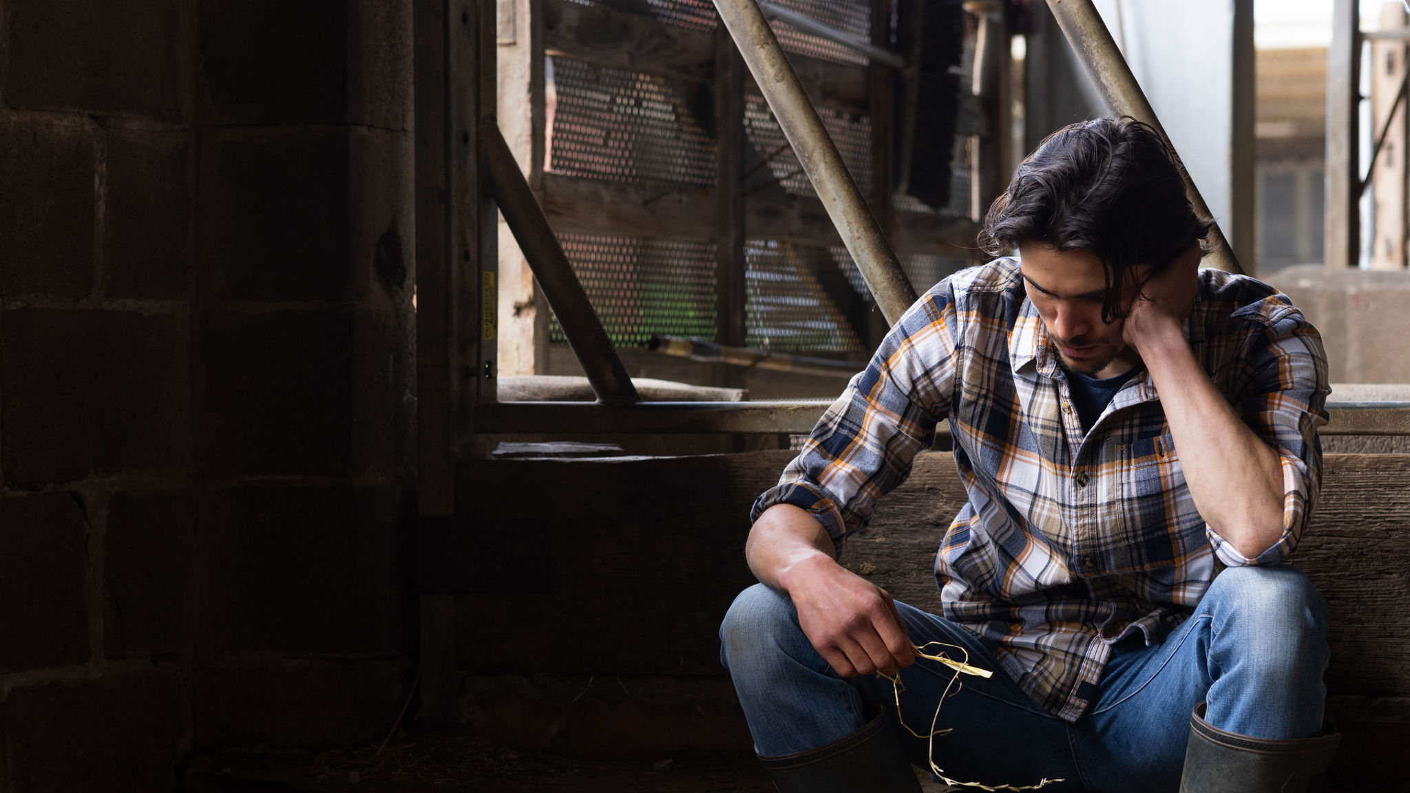 A young farmer sitting with his head in his hands in a barn at the sustainable farm he works at in Embleton, North East England. He is worried about the stress of his job and business.