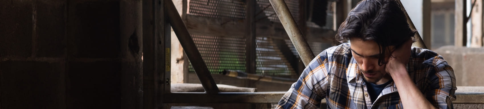 A young farmer sitting with his head in his hands in a barn at the sustainable farm he works at in Embleton, North East England. He is worried about the stress of his job and business.